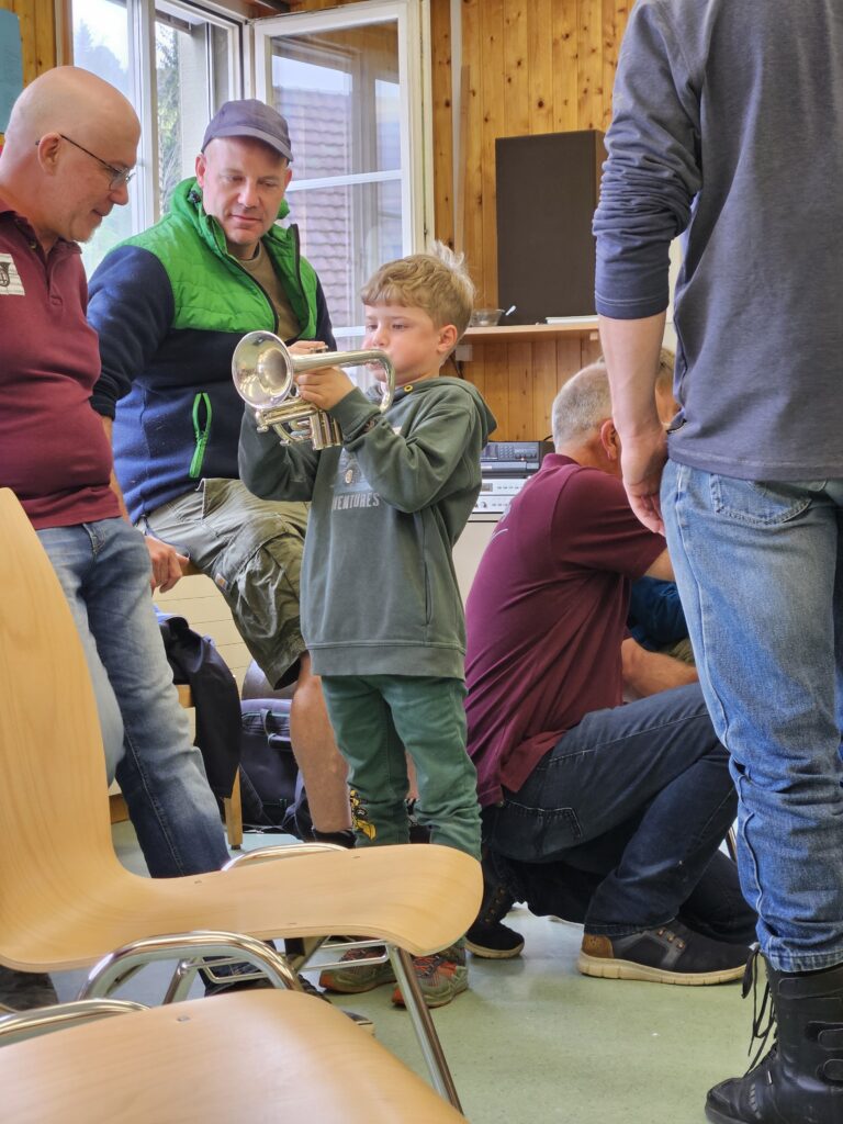 Junge mit Kaki-farbigem Pullover spielt Cornet