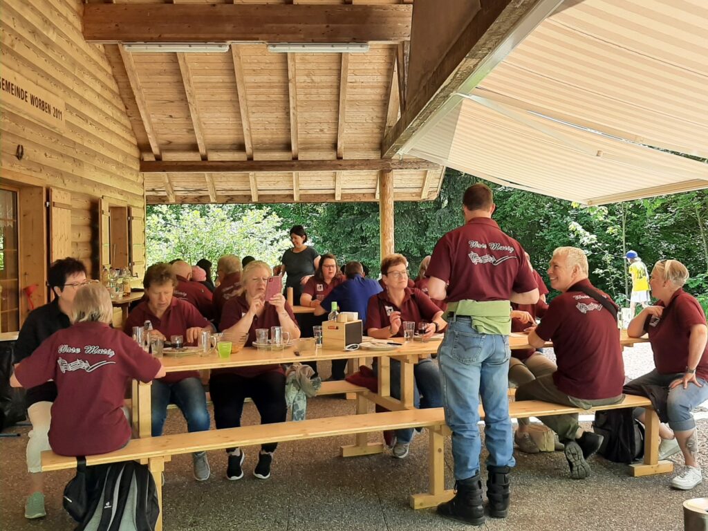 Musikanten sitzen an Tischen und plaudern unter einer Sonnenstore