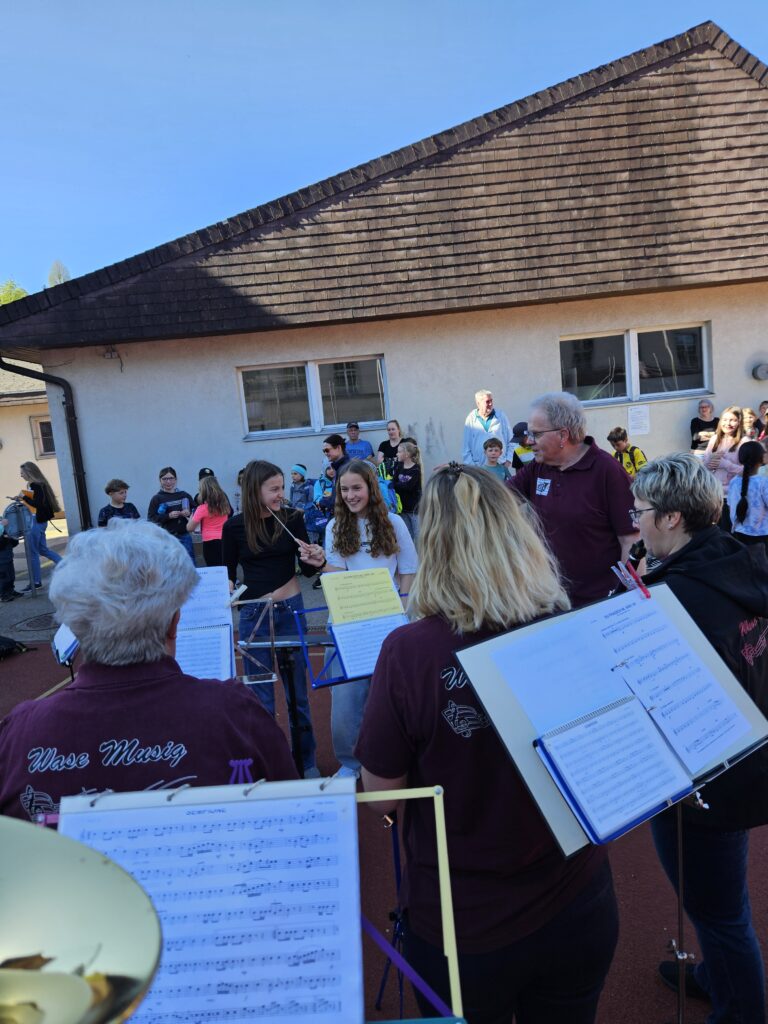zwei Schülerinnen vor der Wase-Musig, eine davon mit Taktstock in den Händen