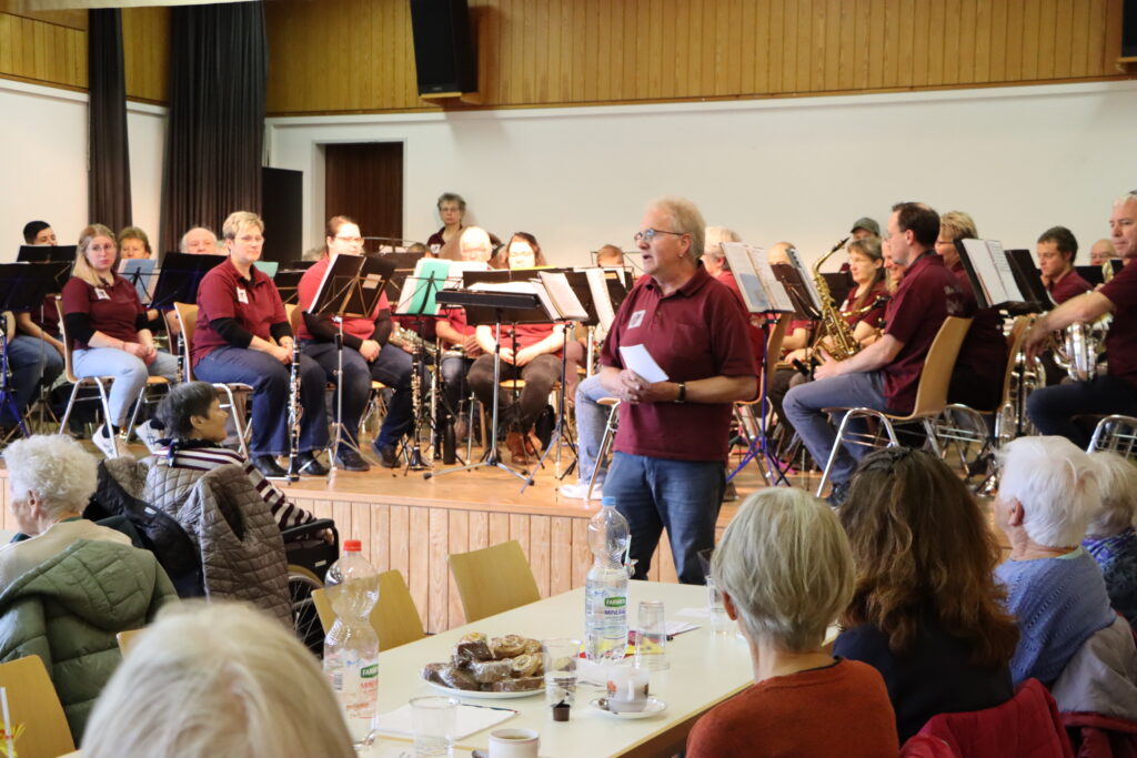 Blick vom Publikum zum Ansager vor der Bühne und den Musikanten auf der Bühne
