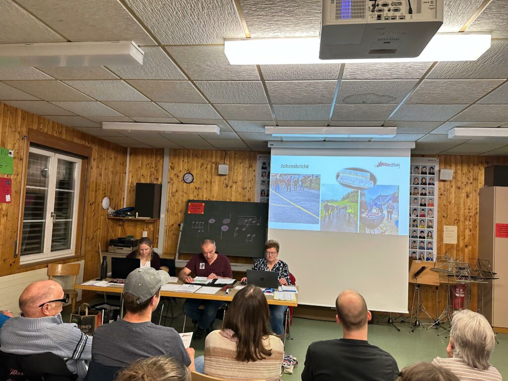 Verammlung und vorne Tisch, an dem Franziska Dubach, Beat Mathys und Caroline Burkhalter (v.l.n.r.) sitzen, rechts eine Leinwand